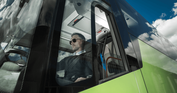 A bus driver buckles a seatbelt in the driver seat of a charter bus